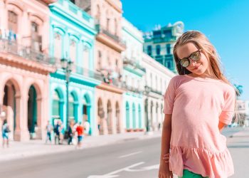 Adorable girl in the street with vintage classic american car in old Havana on Cuba.